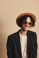 Cute awesome tanned curly man in classic hat brown jacket trendy sunglasses posing isolated on beige pastel background. Fashion New Collection offer. Retro style portrait concept. Free place for ad photo