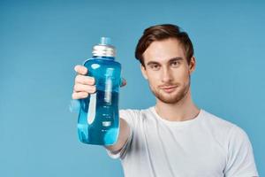sporty man in white t-shirt holding blue water bottle in front of him studio photo