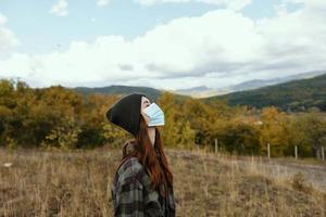 woman in autumn forest in mountains with medical mask on face side view photo