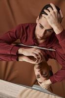 Mirror reflection of a handsome man touches his head with his hand and sit at a table on a fabric background photo
