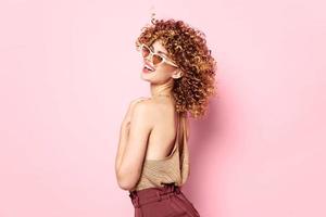 Lady Fun dark glasses curly hair pink background brown pants photo