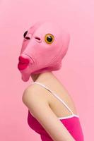 Skinny woman in a pink Halloween costume with a fish head on her face poses funny against a pink background and looks at the camera, art concept photo