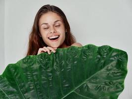 cheerful woman with closed eyes covers herself with a green leaf photo