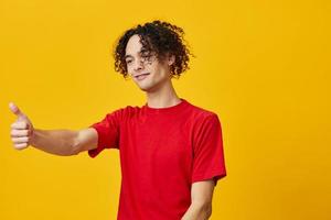 Cheerful funny Caucasian young man in red t-shirt show thumb up gesture posing isolated on over yellow studio background. The best offer with free place for advertising. Emotions for everyday concept photo