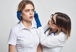 un mujer médico en un médico vestido y azul guantes examina el del paciente cara foto