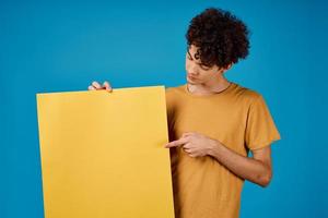 Cheerful guy with curly hair yellow Poster mockup advertising blue background photo