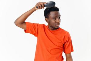 a man of African appearance in an orange T-shirt with a comb in his hands light background photo