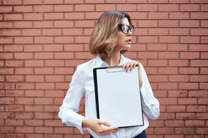 Business woman in white shirt and glasses with documents on the street brick wall photo