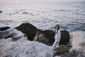 woman stands on rocks in white dress ocean nature travel photo