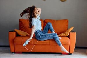 alegre mujer sentado en el sofá a hogar escuchando a música en auriculares inalterado foto