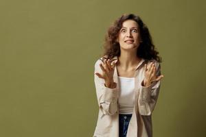 Overjoyed shocked happy curly beautiful female in linen casual shirt gestures while communicating looks at camera posing isolated on olive green pastel background. People Lifestyle Emotions Concept photo