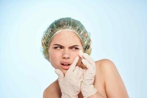 woman with bare shoulders in gloves squeezes out black dots on her face photo