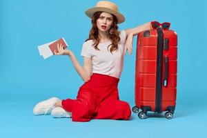 cheerful woman in hat sitting on the floor red suitcase passenger isolated background photo