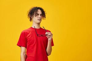 Myopic young student man in red t-shirt funny eyewear can not look afar posing isolated on over yellow studio background. The best offer with free place for advertising. Education College concept photo