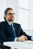 negocio hombre con lentes en un traje trabajos a el computadora en el oficina foto