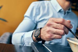 a handsome man with a beard eats borscht in a plate at a table in a cafe and a watch on his hand photo