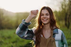 retrato de un joven sonriente mujer en trabajo ropa a cuadros camisa y delantal en naturaleza en el noche después trabajo foto