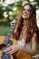 contento hippie mujer con un guitarra relajante en naturaleza sentado en un tartán sonriente y disfrutando el vista. estilo de vida en armonía con naturaleza y yo foto