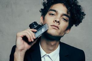 curly-haired man in a jacket and shirt holding a camera in his hand model vogue style photo