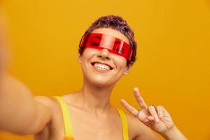 Woman smiling in unusual glasses millennial taking selfies in sportswear against an orange studio backdrop, free space photo