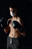 athlete boxing gloves on a black background medical mask on the face naked torso photo