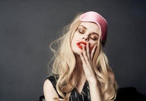 blonde woman smeared makeup on her face on a gray background and a pink sleep mask on her head photo