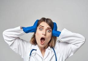 emocional mujer en azul médico guantes toques su cabeza con su manos en un ligero antecedentes foto