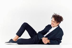 a fashionable guy in trousers and a jacket lies on the floor In a bright room, curly hair sneakers photo