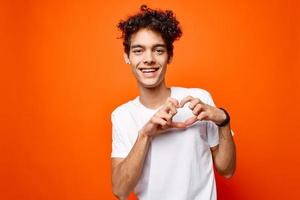 curly guy in a white t-shirt gesturing with his hand on an orange background photo