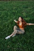 A woman enjoying the outdoors sitting in the park on the green grass in casual clothing with long flowing hair, lit by the bright summer sun without mosquitoes photo