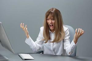 Irritated blonde businesswoman made a critical mistake using desktop computer spread hands sitting at workplace in gray modern office. Remote Job, Technology And Career Profession Concept. Copy space photo