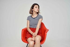 beautiful woman in fashionable clothes sitting on the red chair light background photo