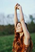 A woman warms up and stretches her arms up in nature in a green park after an outdoor sports workout in the sunset sunlight. The concept of a healthy lifestyle and an athletic body photo