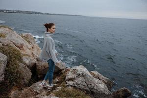 beautiful woman in a gray sweater stands on a rocky shore nature Relaxation concept photo
