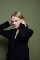 A young charming blonde model tucks her hair behind her ears touches and strokes her curls posing on a green background in the studio photo