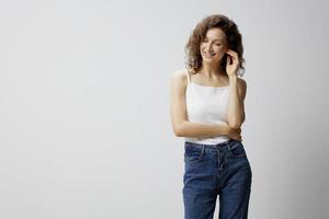 Shy cute happy curly beautiful woman in basic white t-shirt cross hands looks down aside enjoy good mood posing isolated on over white background. People Emotions Lifestyle concept. Copy space photo