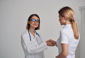 woman doctor in a medical gown shakes hands with a patient in a white t-shirt on a light background photo