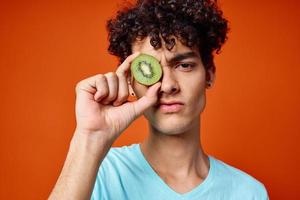 alegre chico con Rizado pelo kiwi cerca el ojos Fruta de cerca foto