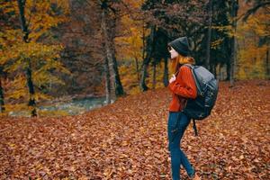 mujer en un sombrero en un rojo suéter y pantalones camina en el parque con un mochila en su espalda viaje turismo otoño paisaje foto