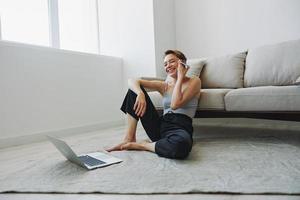 Freelance woman with laptop and phone works from home sitting on the floor in her home clothes with a short haircut, free copy space photo