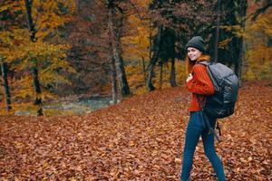 mujer en un sombrero en un rojo suéter y pantalones camina en el parque con un mochila en su espalda viaje turismo otoño paisaje foto