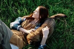 A woman lies on the grass smiling and cuddling her dog in nature in a park in the summer sunset. The concept of health and love for animals, treatment against ticks photo