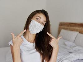 woman in a medical mask on the bed shows her fingers on her face photo