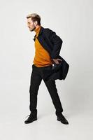 de moda hombre en un naranja suéter en un ligero antecedentes convertido a el lado y pantalones modelo foto