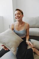 Teenage girl smile everyone sits at home near the couch and tosses up pillows, fun game and happiness without filters, copy place photo