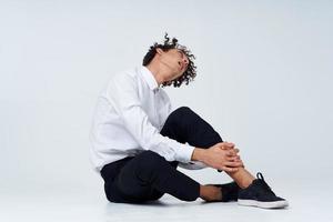 hombre con Rizado pelo en un clásico traje y zapatillas se sienta en el piso y lado ver Copiar espacio foto