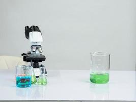 beaker and microscope for scientists was placed on a white wooden table with research reagents in the bright white room for study and work photo