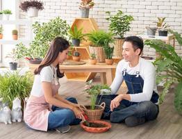 Portrait lovers handsome young man Pretty Asian woman wearing white t-shirt. and apron joking having fun help arrange plant and water plants in small pots In the room arranged plants with love happily photo