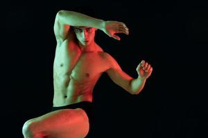 a man athlete with a pumped-up torso raised his leg up on a black background and gestures photo