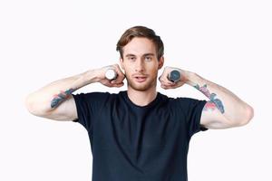 a sporty man in a black t-shirt holds dumbbells near his face on a light background and a black t-shirt photo